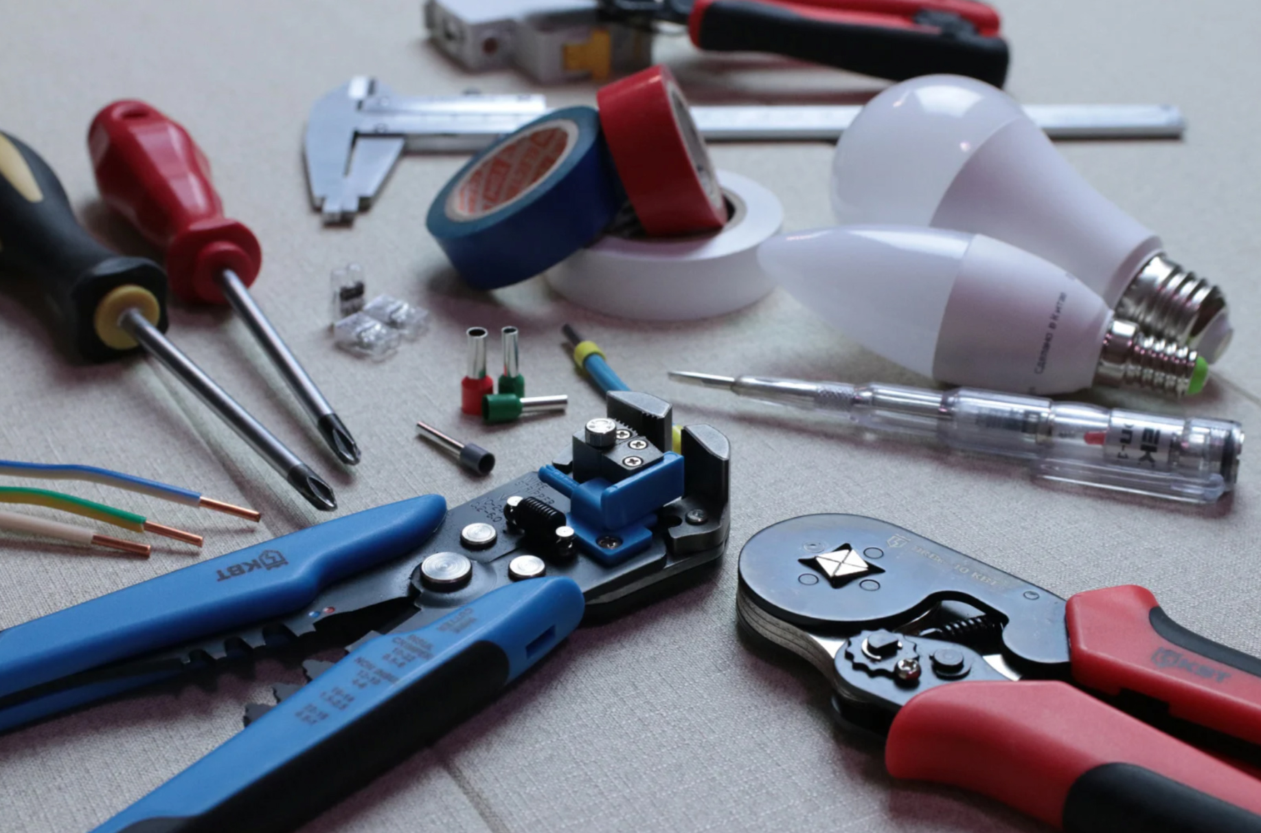 Assorted electrical tools, wires, bulbs, and tape are spread out on a light surface.